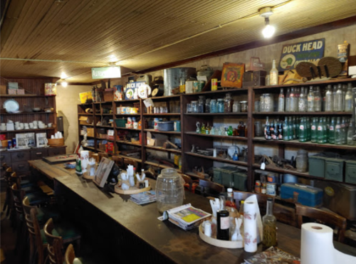 A rustic interior of a vintage store with wooden shelves filled with jars, bottles, and various antiques.