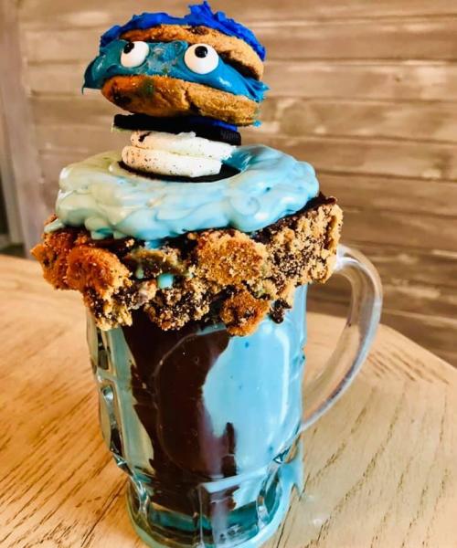 A tall glass filled with blue ice cream, topped with a cookie, chocolate drizzle, and a cookie monster-themed cookie.