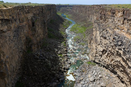 A winding river flows through a deep canyon with steep, rocky walls and lush greenery along the banks.