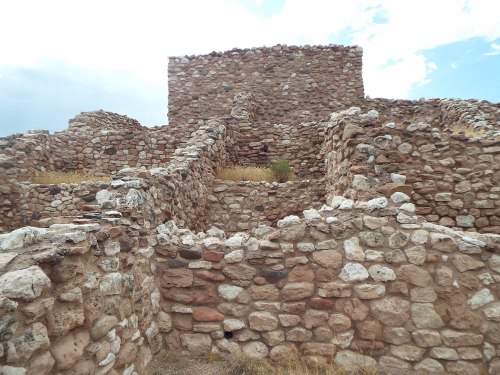 Ancient stone ruins with layered walls and grassy patches under a cloudy sky.