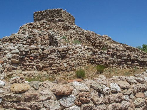 Ancient stone ruins on a hillside under a clear blue sky, showcasing layered rock structures and sparse vegetation.