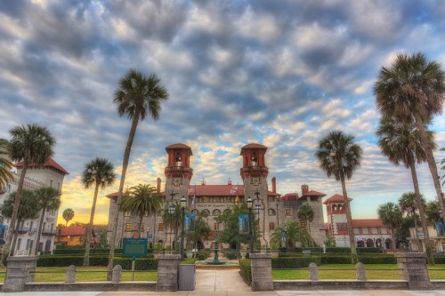 Historic building with towers, palm trees, and a cloudy sky at sunset.