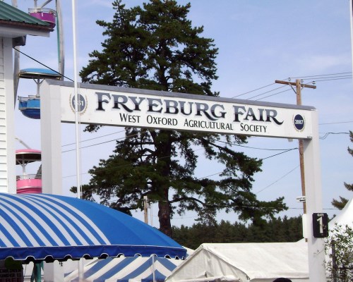 Sign for Fryeburg Fair, West Oxford Agricultural Society, with a blue and white striped tent in the foreground.