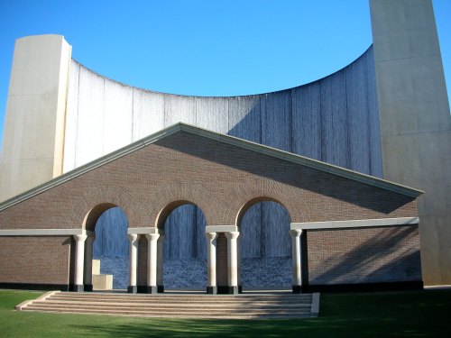 A modern architectural structure featuring a brick building with arches and a large curved wall behind it.
