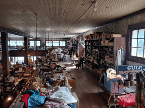 A spacious vintage shop filled with various items, shelves, and cluttered tables under warm lighting.