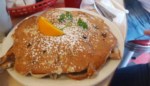 A large pancake topped with powdered sugar, an orange slice, and a sprig of parsley, served on a white plate.