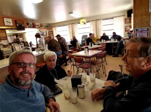 A cozy diner scene with people dining and chatting, featuring a group at a table in the foreground.