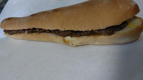A long sandwich filled with ground beef and mustard, resting on a white surface.