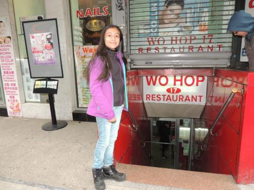 A girl stands outside the entrance of Wo Hop 17 Restaurant, located in a bustling urban area.