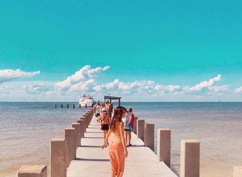 A group of people walking along a pier towards a boat under a bright blue sky with fluffy clouds.