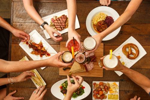 A group of hands toasting with drinks over a table filled with various dishes and appetizers.