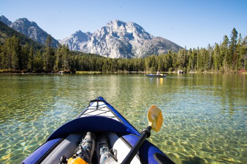 A kayak on a clear lake with mountains and trees in the background, under a bright blue sky.