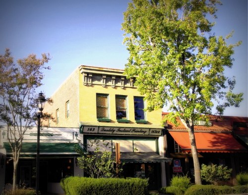 Historic building with green awning and sign, surrounded by trees and shrubs, in a quaint town setting.
