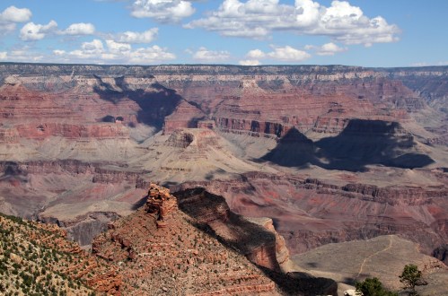 A panoramic view of the Grand Canyon, showcasing layered red rock formations and dramatic shadows under a blue sky.