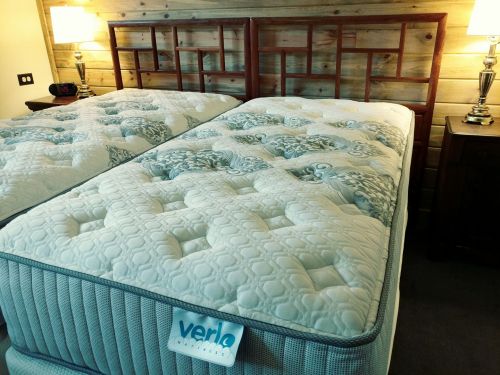 A cozy bedroom featuring two plush mattresses on a wooden bed frame, with bedside lamps and a nightstand.
