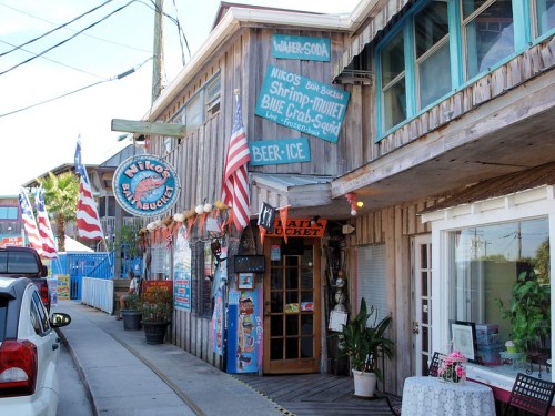 A rustic seafood restaurant with wooden exterior, colorful signs, and American flags lining the entrance.