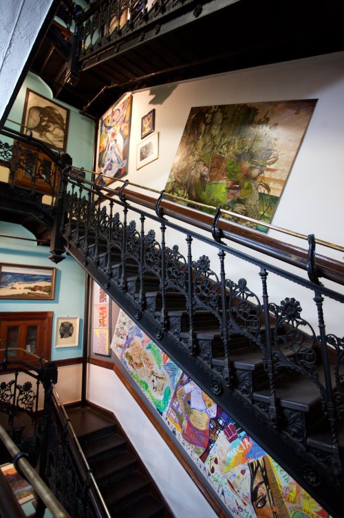 A spiral staircase with ornate ironwork, surrounded by colorful artwork on the walls in a well-lit interior.