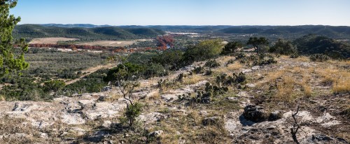 A panoramic view of rolling hills and valleys, featuring rocky terrain and scattered vegetation under a clear blue sky.