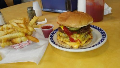 A plate with a stacked cheeseburger topped with pickles and ketchup, alongside a serving of crinkle-cut fries and ketchup.