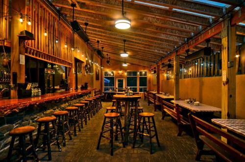 Cozy restaurant interior with wooden beams, bar stools, and tables, illuminated by warm hanging lights.