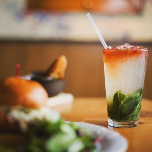 A refreshing layered drink with mint and ice, served in a tall glass, with a burger and salad in the background.