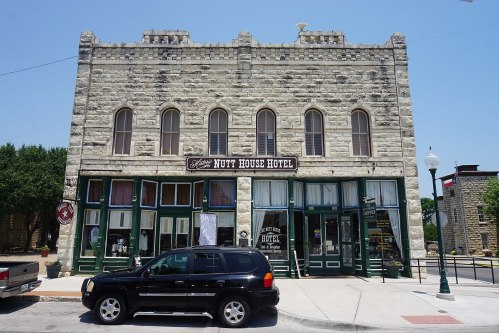 Historic stone building with "Nutt House Hotel" sign, featuring large windows and a parked black SUV in front.
