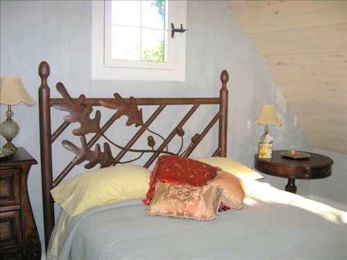 Cozy bedroom with a wooden bed frame, decorative pillows, and a bedside table with a lamp and candle.