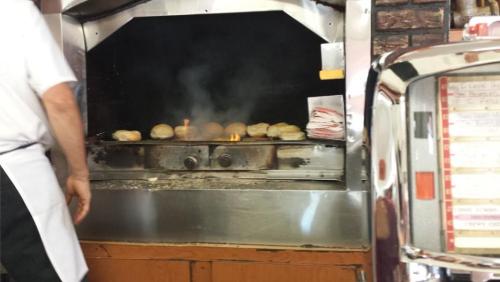 A cook stands by a grill with burgers sizzling and smoke rising in a retro diner setting.
