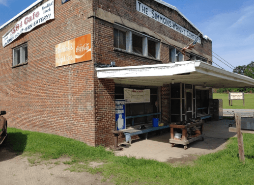 A brick building with a sign for "Simmons & Wright Co." and a cafe, featuring a covered porch and outdoor seating.