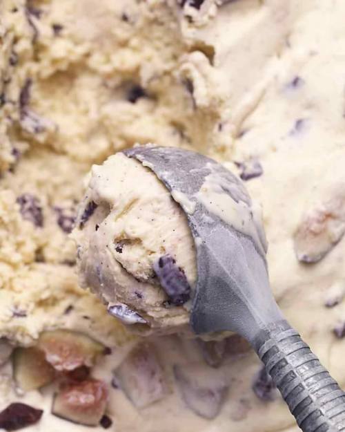 A close-up of a metal ice cream scoop lifting creamy vanilla ice cream with chocolate chunks.