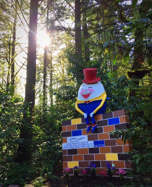 A colorful statue of Humpty Dumpty wearing a top hat, surrounded by trees and sunlight in a forest setting.