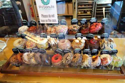 A display case filled with various colorful donuts, each labeled with unique flavors and toppings.
