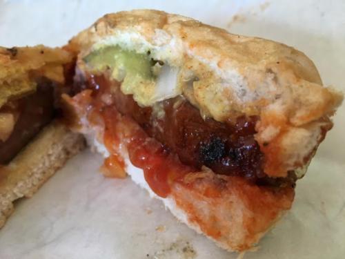 Close-up of a sandwich cut in half, revealing layers of meat, pickles, onions, and sauces on a soft bun.