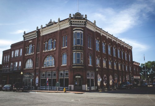 Historic brick building with large windows, ornate details, and a corner location under a blue sky.