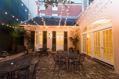 Charming courtyard with string lights, tables, and greenery, featuring brick flooring and French doors.