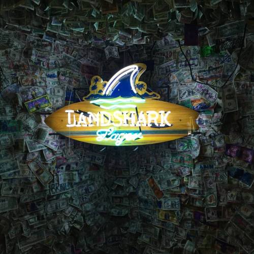 A neon Landshark Lager sign surrounded by a wall covered in various dollar bills.