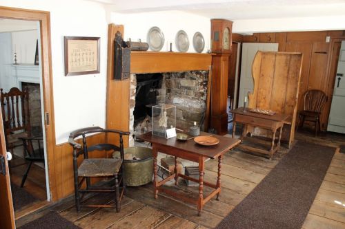 A cozy, historic room featuring a stone fireplace, wooden furniture, and rustic decor on a wooden floor.