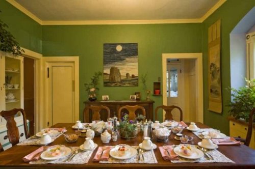 A beautifully set dining table with plates, flowers, and a green wall featuring a moonlit painting.