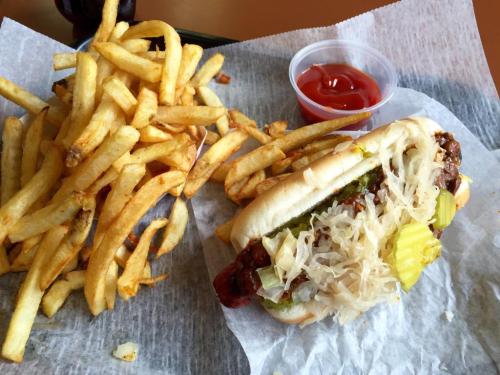 A hot dog topped with sauerkraut, pickles, and onions, served with a side of golden fries and a small cup of ketchup.