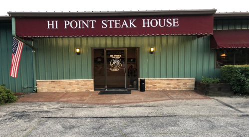 Exterior of Hi Point Steak House with a maroon awning, entrance door, and an American flag nearby.