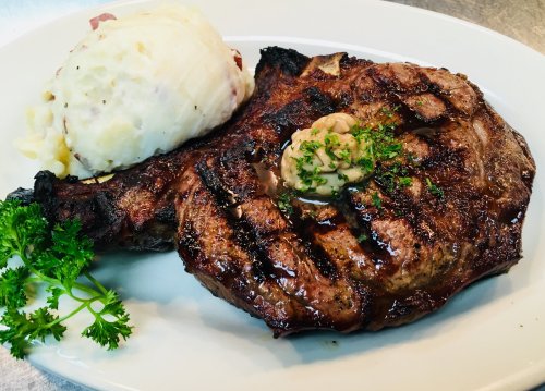 A grilled steak with a dollop of butter and parsley, served alongside creamy mashed potatoes on a white plate.