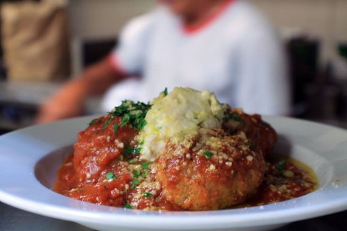 A plate of meatballs in marinara sauce, topped with parsley and served with a side of mashed potatoes.