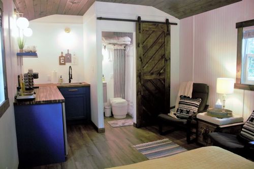 Cozy interior of a small cabin featuring a kitchenette, seating area, and a bathroom with a sliding barn door.