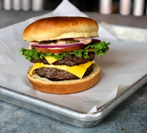 A delicious burger with two beef patties, cheddar cheese, lettuce, onions, and sauce on a toasted bun, served on a tray.