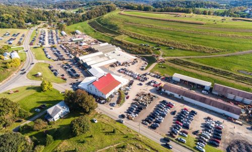 Aerial view of a large parking lot and buildings surrounded by green fields and hills.