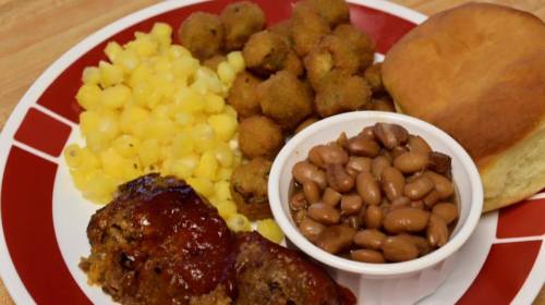A plate of meatloaf with sauce, corn, fried okra, pinto beans, and a biscuit.