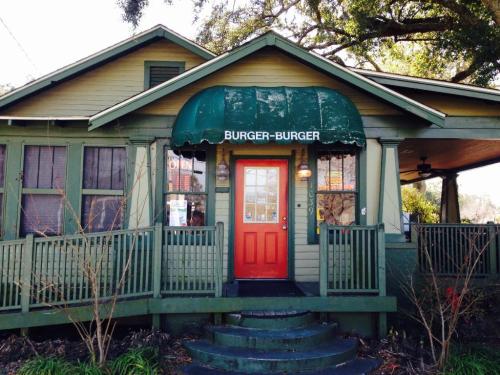 A green house with a sign reading "Burger-Burger" and an orange door, surrounded by trees and a porch.