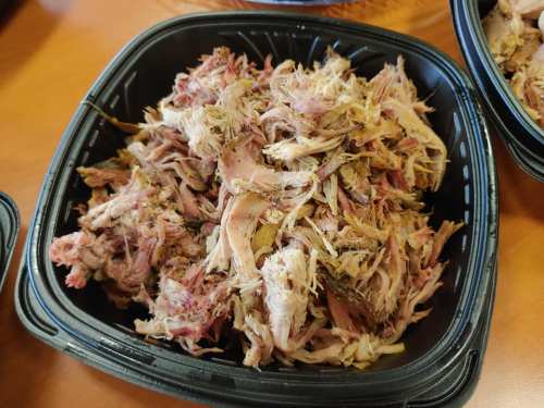 A black container filled with shredded, cooked meat, likely pulled pork, on a wooden table.