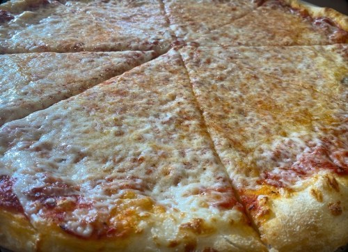 A close-up of a cheese pizza with golden crust and melted cheese, sliced into triangular pieces.