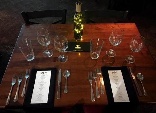 A dining table set for a meal, featuring menus, glasses, utensils, and a decorative bottle with lights.